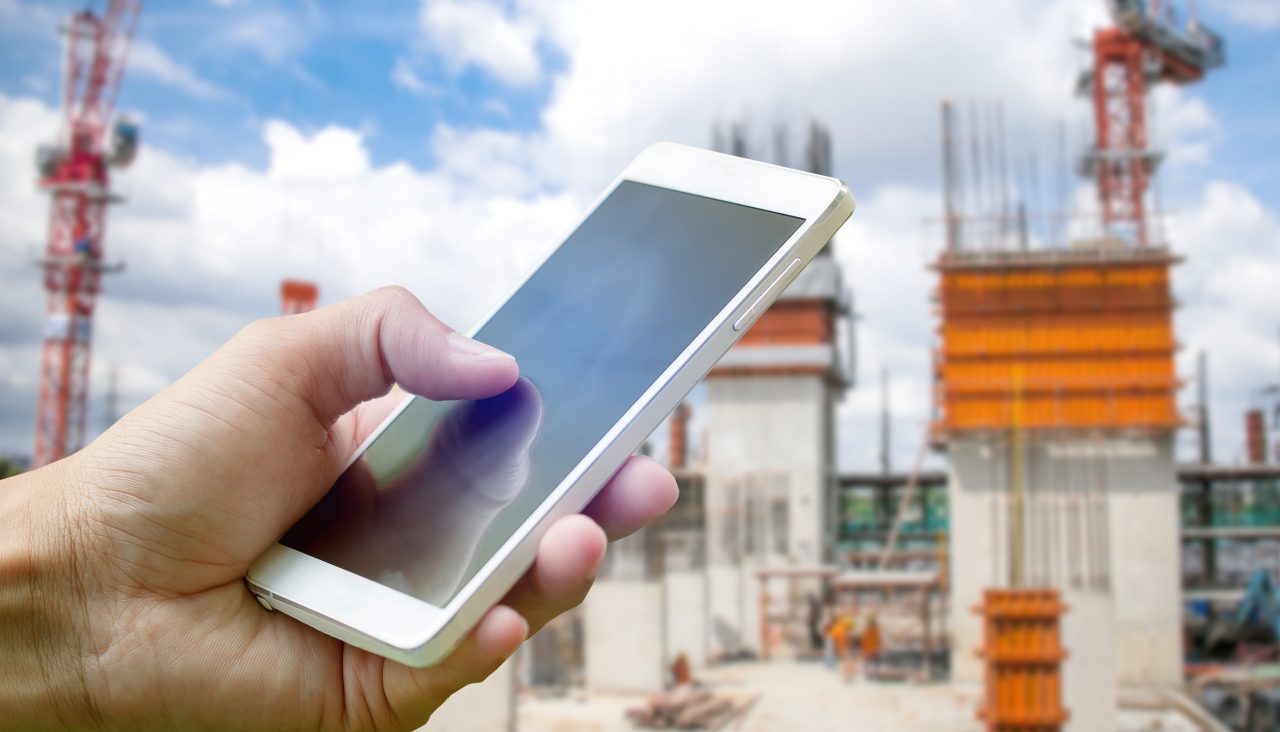 Hand holding smartphone on blurred construction site workers with cloud and blue sky; Shutterstock ID 501239134; Purchase Order: Website Bilder Janet Hanke; Client/Licensee: Hilti Deutschland AG